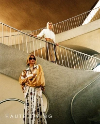 Two female models posing on a curved architectural staircase in modern fashion apparel for an editorial shoot.