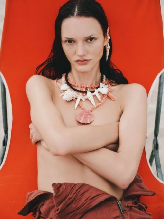 A model poses on a beach chair wearing a shell necklace and earring, with a close-up shot emphasizing summer fashion and seaside aesthetics.