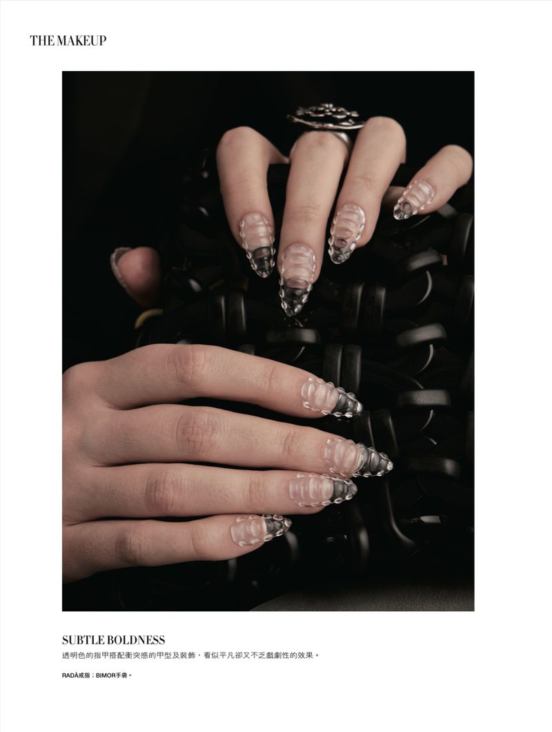 Fingernails with a clear, ribbed, segmented design, ring on finger, against a black background. Beauty and fashion concept.