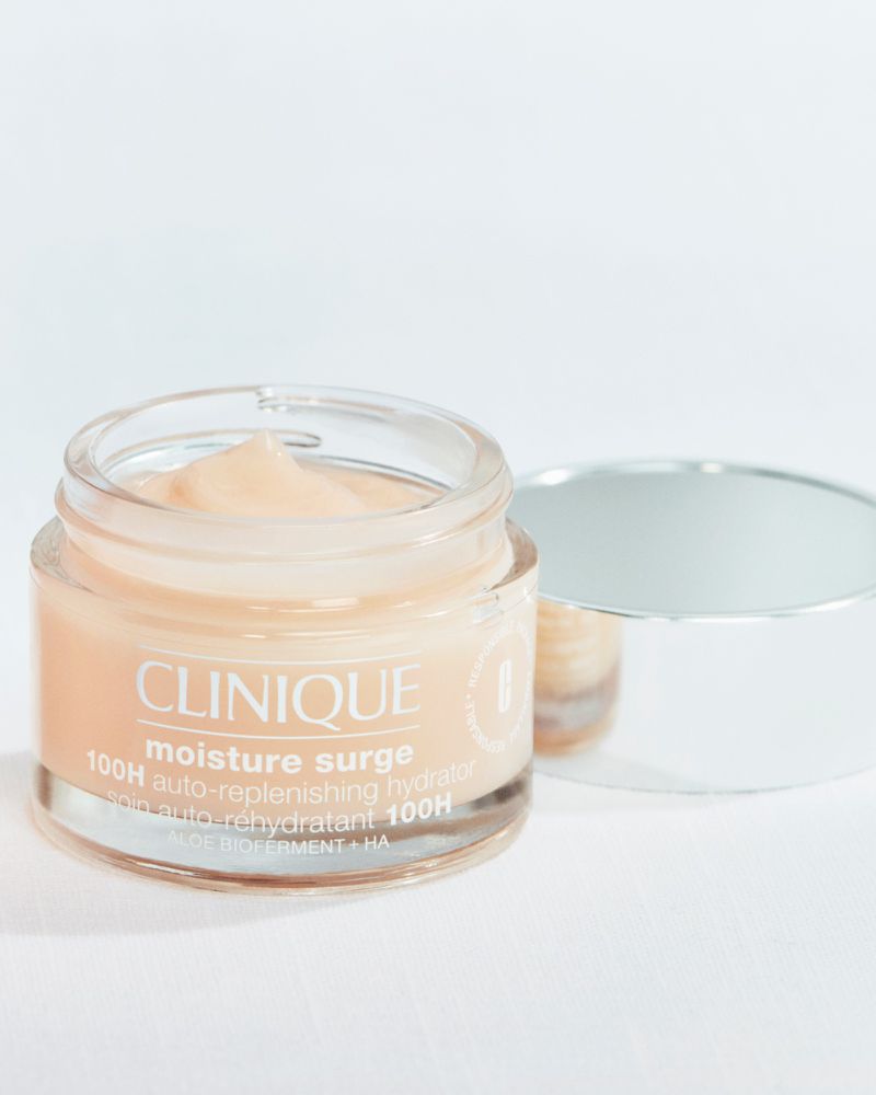 Clinique Moisture Surge 100H auto-replenishing hydrator in a clear jar with a silver lid on a white surface, promoting skincare and beauty.