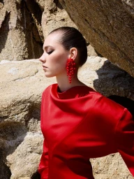 Profile of a model in a vibrant red top and statement red beaded earrings posing against a textured rocky background