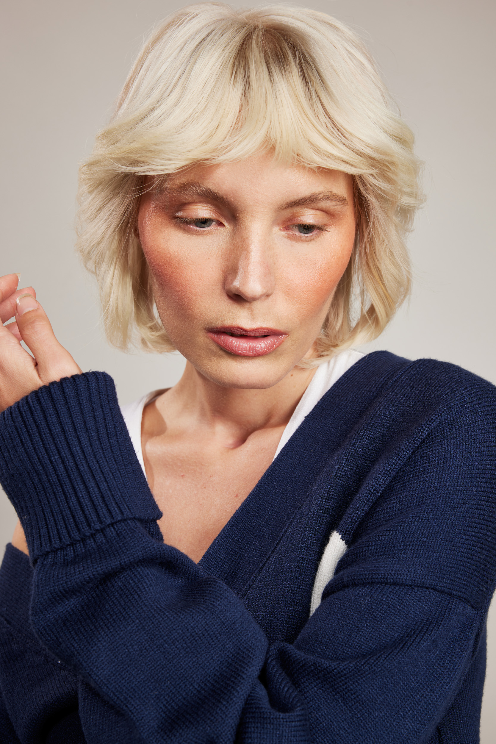 Blonde woman in dark-blue cardigan poses in a studio with fair complexion and light make-up. Fashion and beauty photography.