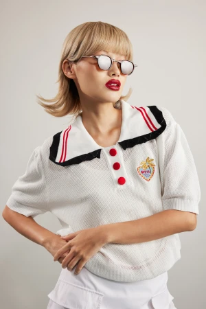 Model in white polo shirt with red buttons and metallic sunglasses against a plain grey studio backdrop for CPR Hair.
