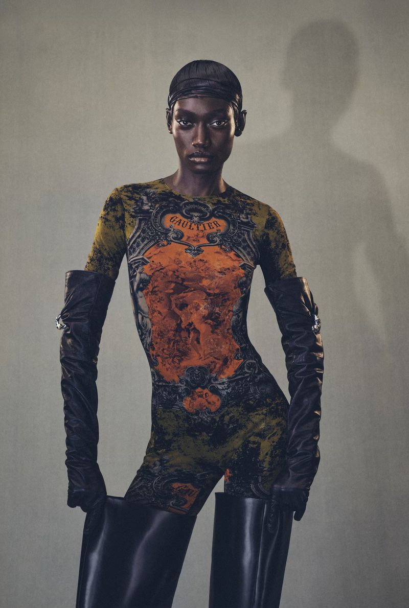 Fashion shot of an adult woman wearing a Jean Paul Gaultier print catsuit and black over-the-knee boots in a studio setting.
