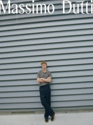 Model Jonas Glöer in striped polo and dark trousers leaning against a grey paneled wall for Massimo Dutti