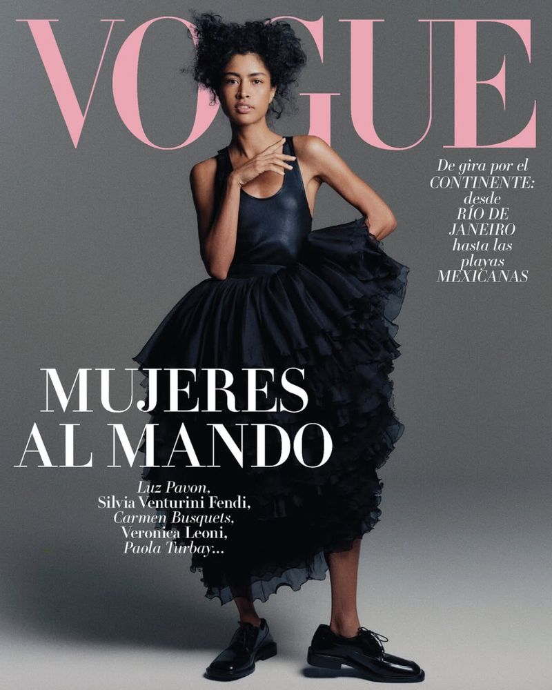 Vogue cover featuring a model wearing a black dress and black shoes against a grey background with pink 'Vogue' text.