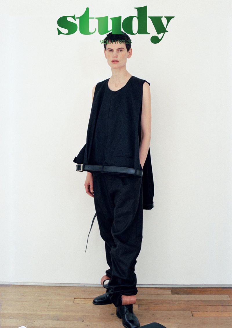 Fashion model poses in black top and pants against a white wall backdrop, with green 'study' text at the top of the frame.