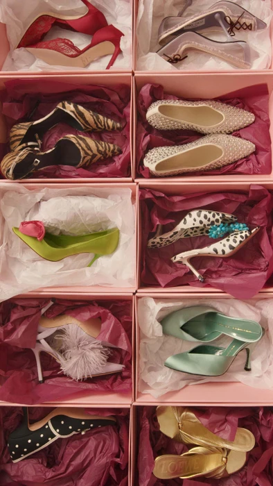 Top-down view of pink shoeboxes filled with various designer high heels resting on tissue paper.