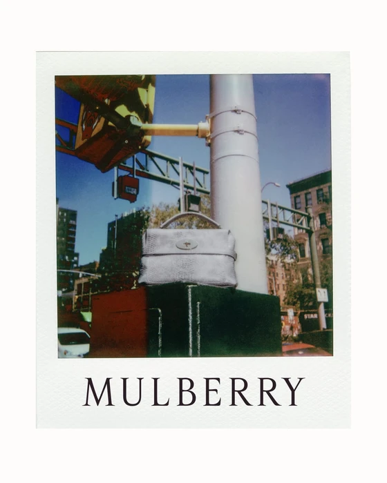 Polaroid photograph of a silver leather handbag resting on a concrete structure with a city street background and Mulberry text below.