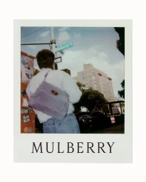 Polaroid-style photograph of a person wearing jeans and a white top with a purple Mulberry handbag on Mulberry St.