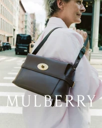Woman wearing a light pink shirt and carrying a dark brown leather shoulder bag on a city street
