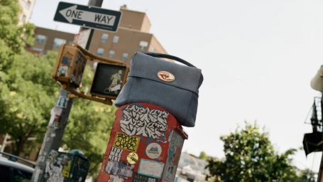 Blue leather handbag resting on a red sticker-covered post beneath a street sign outdoors.