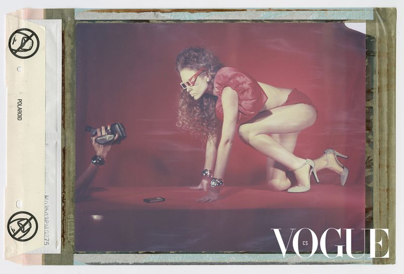 A model in red loungewear poses in an indoor studio, shot with a camcorder in the foreground, inside a Polaroid frame for a fashion editorial.