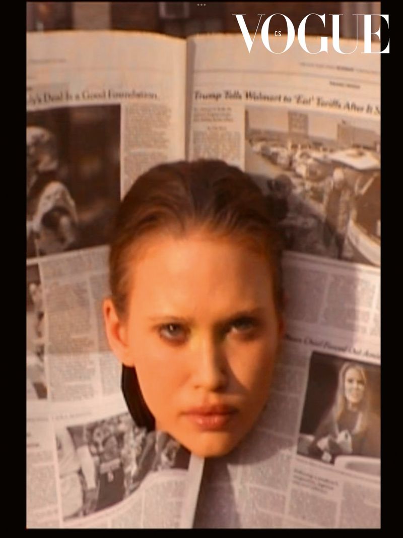 Portrait of a woman surrounded by newspapers, featuring the 'Vogue' logo, neutral skin tone, and focused facial expression.