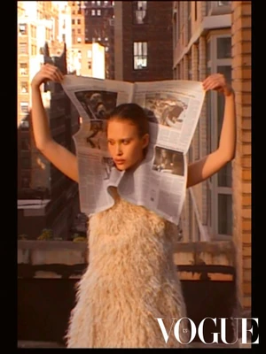 Model Arina Maksimova holding up an open newspaper framing her head against a brick building exterior in a Vogue Czechoslovakia editorial.