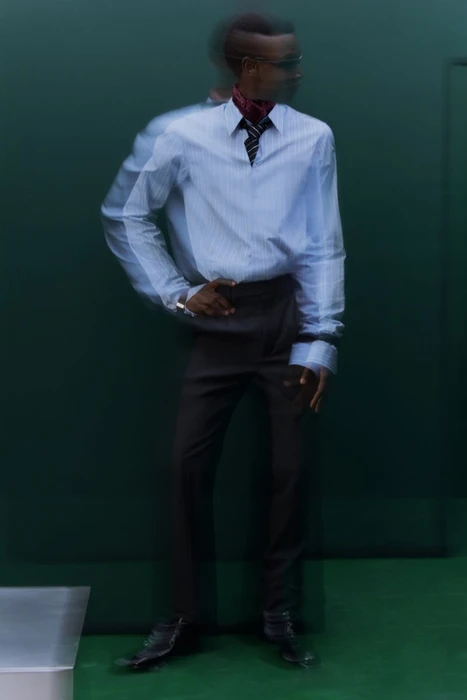 Model wearing a striped dress shirt and dark trousers with motion blur against a dark green backdrop