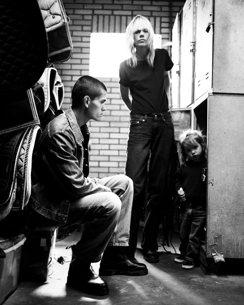 Black and white portrait of three individuals in casual attire posing near lockers and equipment in a dimly lit room. Editorial photography.