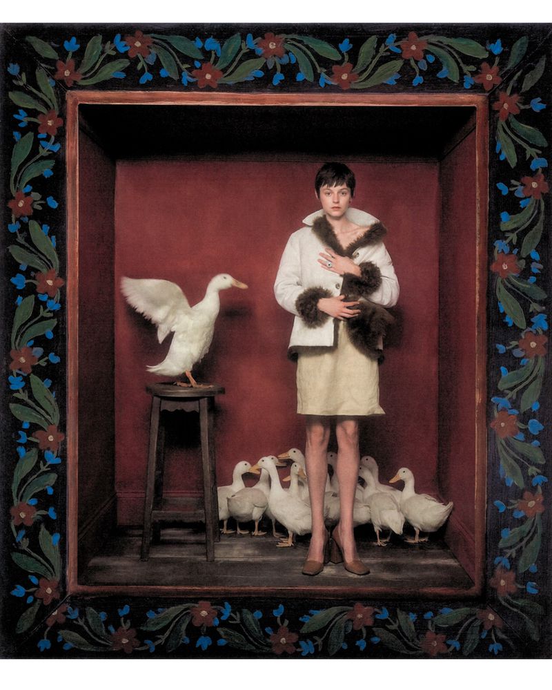 Actor Emma Corrin standing inside a dark red box surrounded by white ducks for Harper's Bazaar UK photographed by Szilveszter Mako