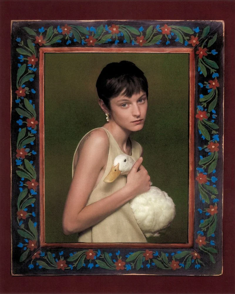 Portrait of Emma Corrin holding a white duck within an ornate painted floral frame for Harper's Bazaar UK.