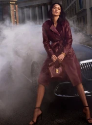 Kendall Jenner wearing a burgundy leather coat leaning on a classic car amidst smoke on a city street.