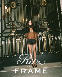 Charlotte Lawrence standing in front of ornate iron gate wearing brown and black windbreaker jacket