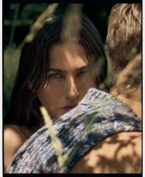 Close-up portrait of a woman looking past another person's shoulder outdoors among tall grasses in natural sunlight