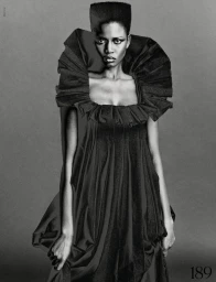 Model Ajah Angau Jok in a black ruffled dress with a flat-top high hairstyle against a grey studio background.