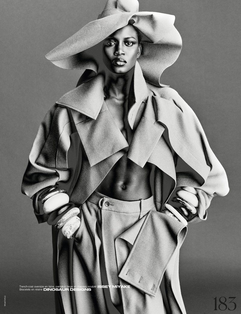 Model Ajah Angau Jok wearing a wide-brimmed hat, structured coat, and bangles in a black and white editorial shoot by Mikael Schulz.