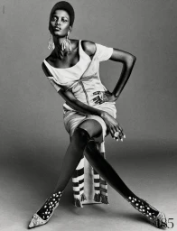 Model Ajah Angau Jok wearing a structured dress and tall boots seated against a grey backdrop for French Magazine