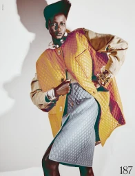 Model Ajah Angau Jok in a quilted yellow vest and grey skirt with bold accessories against a white studio background.