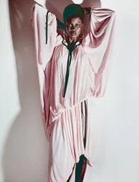 Model Ajah Angau Jok in a voluminous pink dress with dark ribbons against a white backdrop for French Magazine