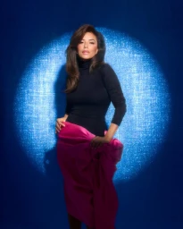 Eva Longoria in a black turtleneck and magenta skirt standing before a textured blue circular spotlight backdrop
