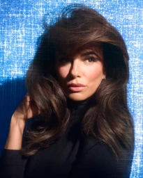 Eva Longoria with voluminous dark brown hair and black top against a sparkling textured blue background
