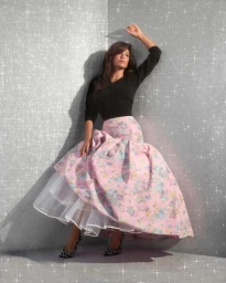 Eva Longoria wearing a black top and a voluminous pink floral skirt against a glittering silver studio backdrop.
