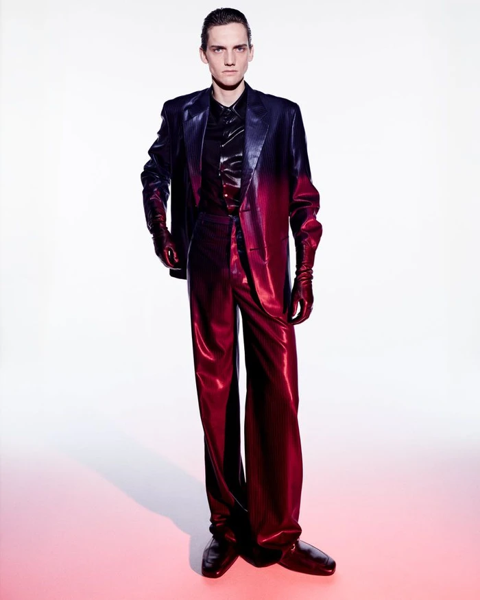 Model wearing a gradient red and black suit standing against a white backdrop