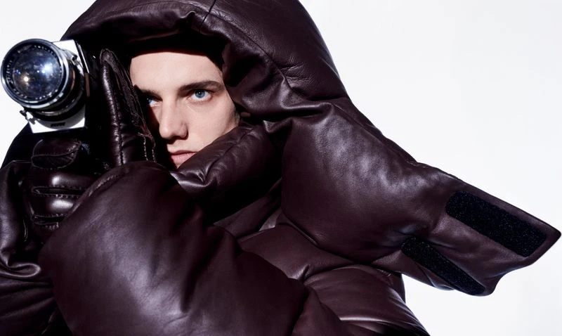 Model Tijs van der Gun wearing a dark puffy leather jacket holding a vintage camera by photographer Marc de Groot