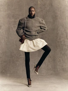 Model Nyibol Dok Jok wearing a grey sweater, white bubble skirt, and stirrup pants for Glamour Germany