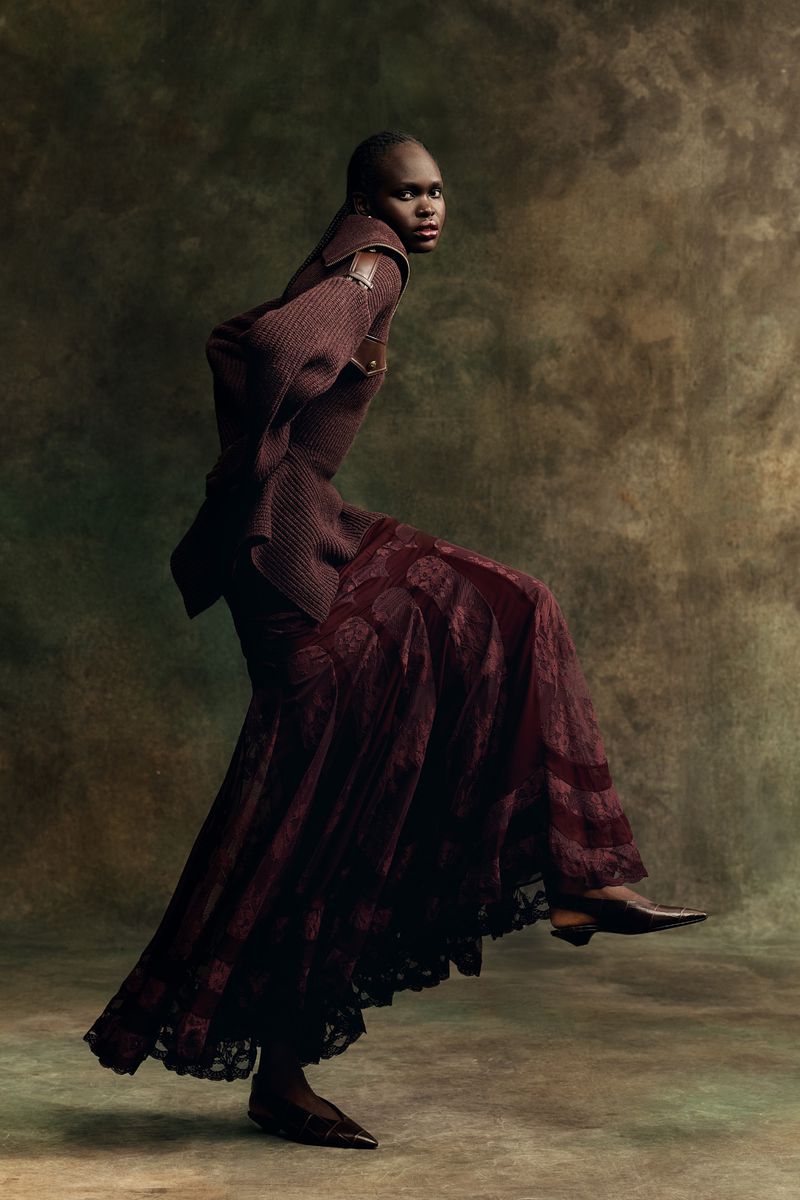 Model Nyibol Dok Jok wearing a ribbed burgundy top and patterned long skirt against a textured backdrop
