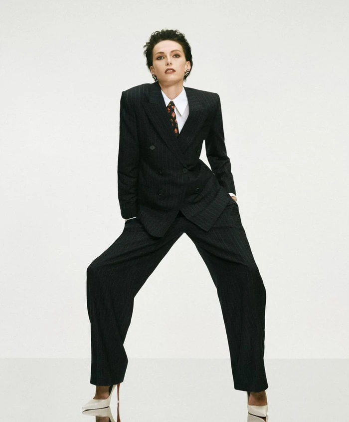 Model Alex Consani wearing a dark pinstripe pantsuit and white shirt against a white seamless background for WSJ The New Sexy editorial.