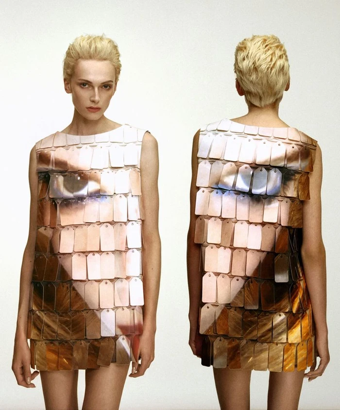 Model Alex Consani wearing a shimmering sequined dress with a printed eye design against a white studio background.