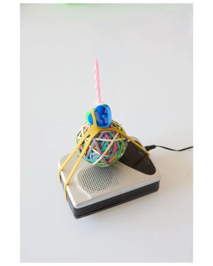 Rubber band ball with a birthday candle on a small electronic device against a white background