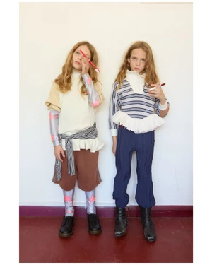 Two young models posing against a white wall wearing layered clothing and holding red objects for i-D Magazine