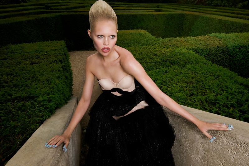 Woman in couture dress poses in garden maze. Elegant fashion shot with model in black gown and maze background.