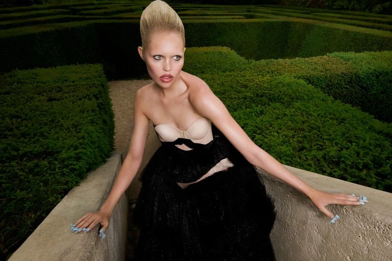 Woman in couture dress poses in garden maze. Elegant fashion shot with model in black gown and maze background.