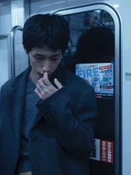 Man wearing a charcoal grey coat and dark shirt standing inside a train car with a blue-toned color grading.