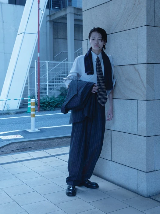 Model in pinstripe suit and dotted tie leaning against stone pillar outdoors for WSJ Strong Suit project