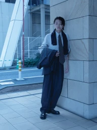 Model in pinstripe suit and dotted tie leaning against stone pillar outdoors for WSJ Strong Suit project