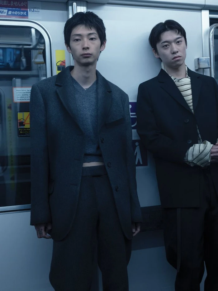 Two men in dark suits standing inside a subway train car for a WSJ editorial photographed by Takashi Homma