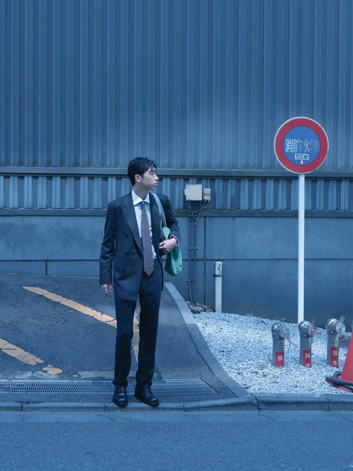 Man in a dark suit standing on a street next to a traffic sign for WSJ Strong Suit editorial