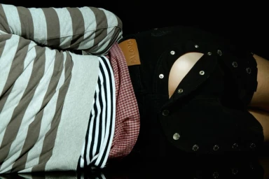 Model lying down wearing a striped sweater and black shorts with snap button details for Fucking Young